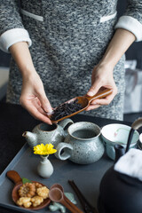 A woman showing a spoon with dry tea leaves.