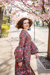 Sakura branches with flowers on a tree in the streets of the city. Happy woman girl spinning on the street with blooming sakura. Sakura blossoms.