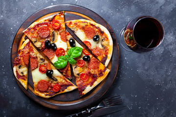 Homemade italian pizza with mozzarella, pepperoni sausages, olives and basil and a glass of red wine on the table top view