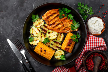 Grilled chicken breast with corn and zucchini on a grilled pan top view. Summer dish with grilled chicken and vegetables.
