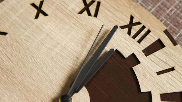 The second, minute, and hour hands on the wooden wall clock with Roman numerals approach twelve o'clock. Seconds tick by, and the hands indicate 12 o'clock, noon, or midnight. New Year, Christmas.