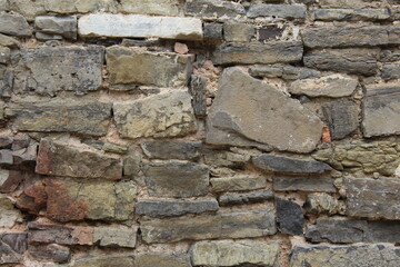 An old, ancient wall of weathered stones and bricks in a gray tone.