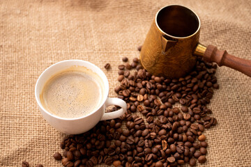 Cup of coffee and cezve with coffee beans on rustic rag. Vintage turk with roasted beans.