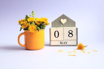 Calendar for May 8: cubes with the numbers 0 and 8, the name of the month of May in English, a bouquet of dandelions in a yellow cup on a light background