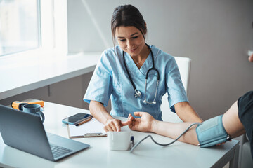 Charming female doctor checking patient blood pressure in clinic