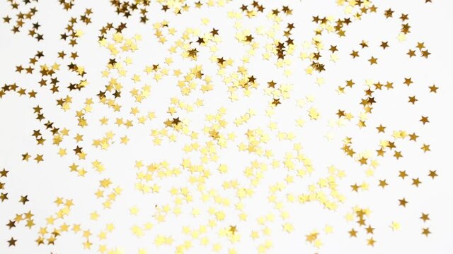 Golden, glittering stars shimmer on a white background. Sequin pattern, festive background