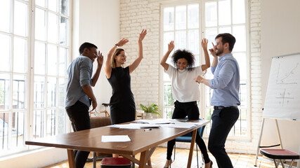 Overjoyed millennial diverse mixed race business people dancing in modern office, celebrating...