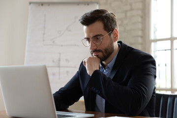Thoughtful young male ceo executive manager in eyeglasses working on successful online project,...