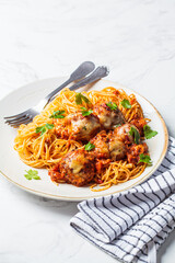 Spaghetti with meatballs, cheese and tomato sauce in white dish.