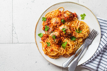 Spaghetti with meatballs, cheese and tomato sauce in white dish, top view.