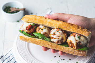Sub meatballs sandwich with cheese, spinach and tomato sauce in baguette in hand.