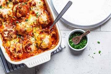 Baked cheesy meatballs casserole with tomato sauce in the oven dish, top view.