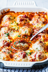 Closeup of baked cheesy meatballs casserole with tomato sauce in the oven dish.
