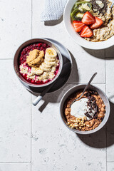 Flat lay of assorted oatmeal bowls with chocolate, fruit, berry and yogurt, gray tiles background, top view. Healthy breakfast concept.