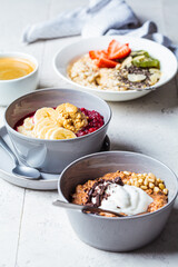 Assorted oatmeal bowls with chocolate, fruit, berry, yogurt and coffee, gray tiles background....