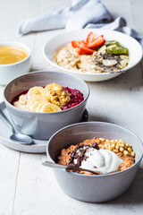 Assorted oatmeal bowls with chocolate, fruit, berry, yogurt and coffee, gray tiles background. Healthy breakfast concept.