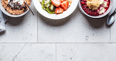 Frame of oatmeal bowls with chocolate, fruit, berry and yogurt, gray tiles background, copy space. Healthy breakfast concept.