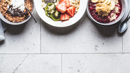 Frame of oatmeal bowls with chocolate, fruit, berry and yogurt, gray tiles background, copy space. Healthy breakfast concept.