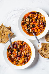 Flat lay of italian beans soup with sausages in white plate, top view, white marble background.