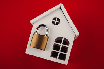 White model of house with lock shut off on red background. Alarm and security concept