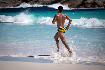 A young fit, tanned male athelete in bathers jogs along the pristine beach at Victoria Harbor in the Cape LeGrande National Park.