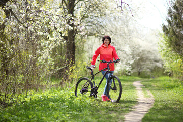 Beautiful woman on a bike in a blooming spring garden. Beautiful mature woman posing for the camera in a blooming spring garden. 