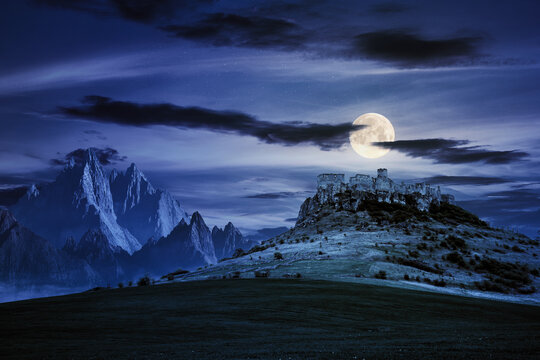 castle on the hill at night. composite fantasy landscape. grassy meadow in the foreground. rocky peaks of the ridge in the distant background in full moon light