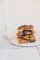 Stack of homemade oatmeal scones with berries stacked on white plate and glass of plant based milk. Vegan sweet baked food. Gluten free pastry. Healthy breakfast.