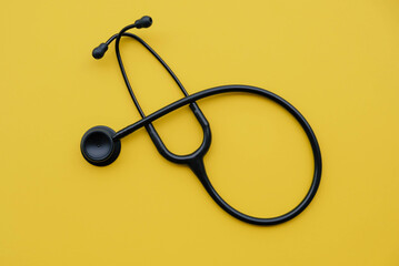 Black medical stethoscope on yellow background. Medicine and healthcare concept. Space for text. Flat-lay, top view.