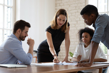Young female team leader analyzing sales statistics in paper report with mixed race colleagues at...