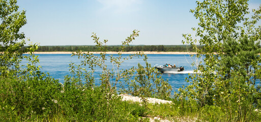 beautiful green bank of the Volga river and the boat rushes in the distance on the water