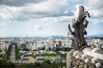 Obraz premium Koi carp Tiger headed fish statue on roof top of Himeji Castle with view of Himeji City (soft focus), Japan