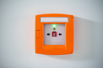 An orange fire button behind the glass on a white wall