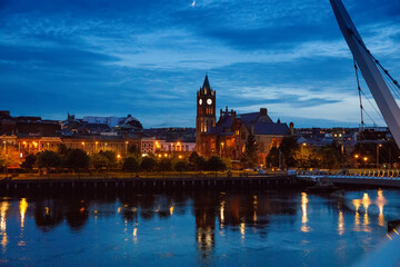 Derry, Ireland. Illuminated Peace bridge in Derry Londonderry, City of Culture, in Northern Ireland with city center at the background. Night cloudy sky with reflection in the river at the dusk