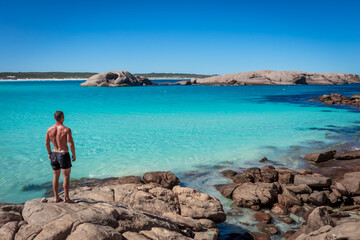 Landscape view of an athletic young man viewing the pristine white sands, crystal clear aqua water and granite boulders on a clear blue day at Twilight Cove, near Esperance in Western Australia.