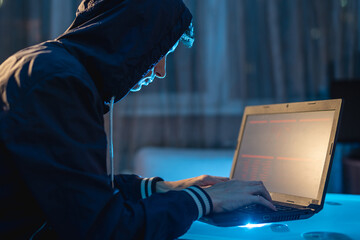 Cybercriminal in the hood typing program code while stealing access databases with passwords....