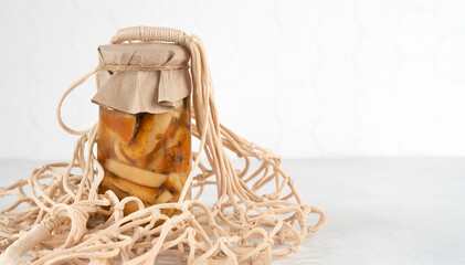 Zero waste eco friendly reusable shopping bag. Marinated pickled edible mushrooms boletus edulis in glass jars in white mesh cotton bag on white kitchen table. Homemade preserves of mushrooms.
