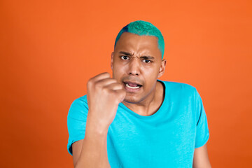 Black african man in casual on orange background blue hair shouting angry raising fist unhappy and...