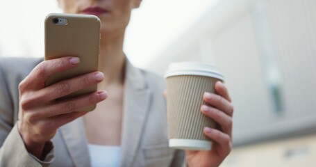 Close up of the famale hand scrolling and taping on the smartphone. Blonde woman in glasses drinking coffee on the blurred background. Outdoor