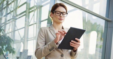 Portrait of the Caucasian beautiful businesswoman, taping on the tablet computer, smiling to the...