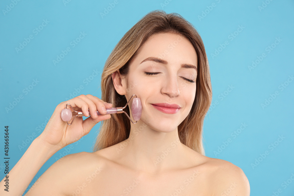 Sticker Young woman using natural rose quartz face roller on light blue background