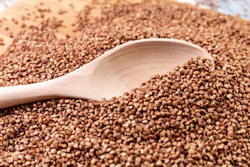 Scattered buckwheat. Buckwheat in a wooden spoon lies on a wooden table. Healthy eating. Diet food. Close-up. High quality photo