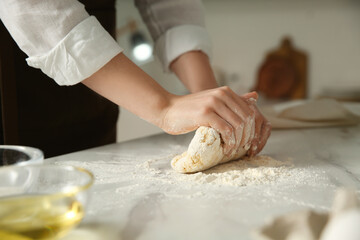 Woman kneading dough at table in kitchen, closeup
