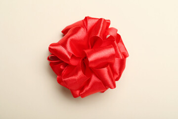 Red ribbon bow on beige background, top view