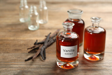 Aromatic vanilla extract and dry pods on wooden table, space for text
