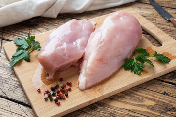Raw chicken breast fillet on a wooden chopping board. Wooden rustic background.