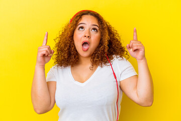 Young latin curvy woman listening music isolated on yellow background pointing upside with opened mouth.