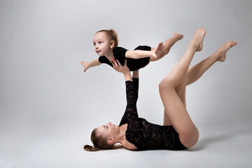 Mother lying down holding her daughter, she raised her hands imagining herself an airplane who loves to fly in the air