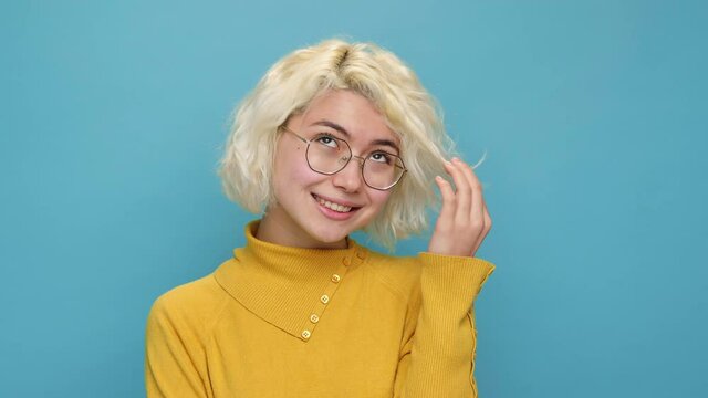 Portrait coquettish cute asian young woman face close up twists lock of curly hair at her face embarrassed smiling looks at camera on blue background. Teen girl feel happy Positive emotions Lifestyle