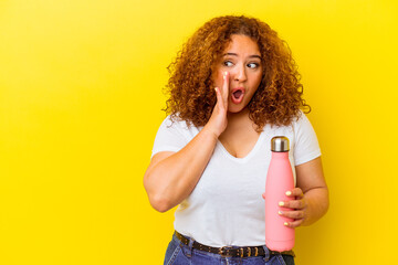 Young latin woman holding a thermos isolated on yellow background is saying a secret hot braking news and looking aside